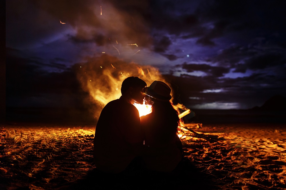 Pareja besándose en la noche en una playa frente a una fogata